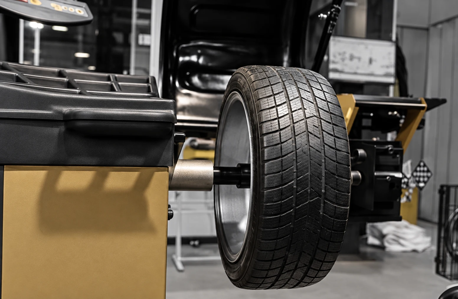 Tyre mounted on a wheel-balancing machine with charcoal and muted gold panels.